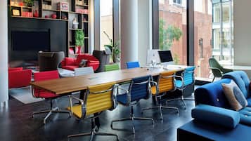 Una sala de reuniones moderna con una mesa grande, sillas coloridas, un sofá azul y una estantería con libros y objetos decorativos.