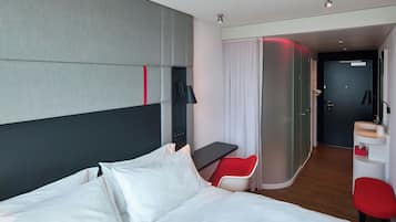 Een moderne hotelkamer met een groot bed, een bureau, een rode stoel en een zithoekje.