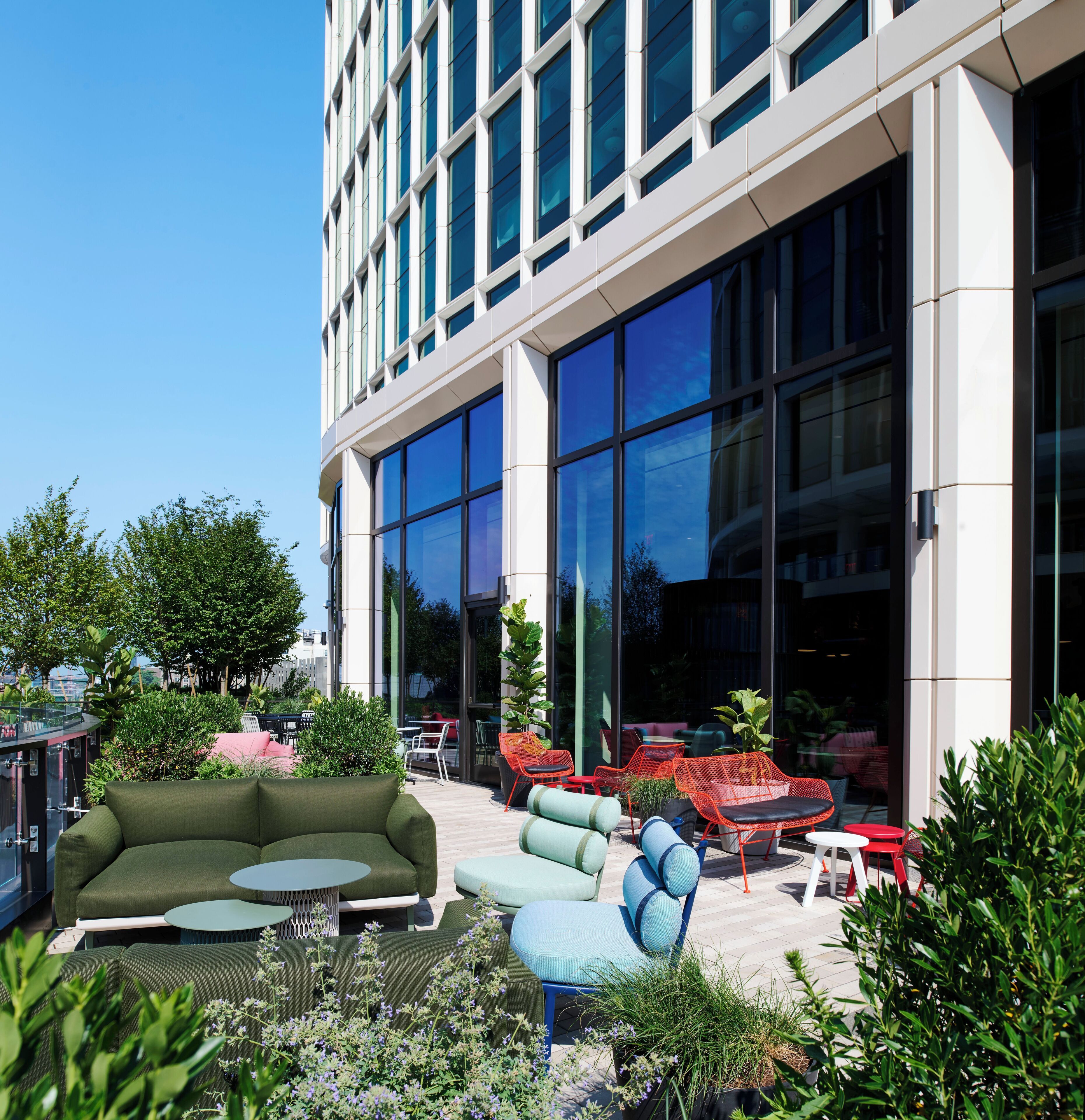 An outdoor seating area with modern furniture, large windows, and greenery.