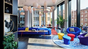 A modern lobby with a blue sofa, colorful ottomans, and a large window with a city view.
