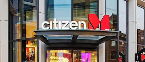 Das Hotel von außen, mit einer Glasfassade, einem gut sichtbaren Schild 'Citizen Hotel' und einem Glastür-Eingang.