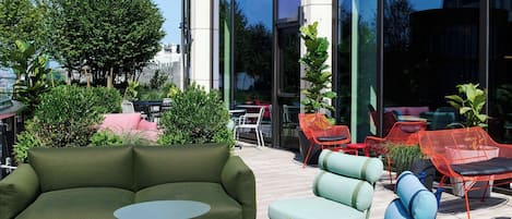 Un área de estar al aire libre con un sofá verde, una silla azul y sillas rojas.