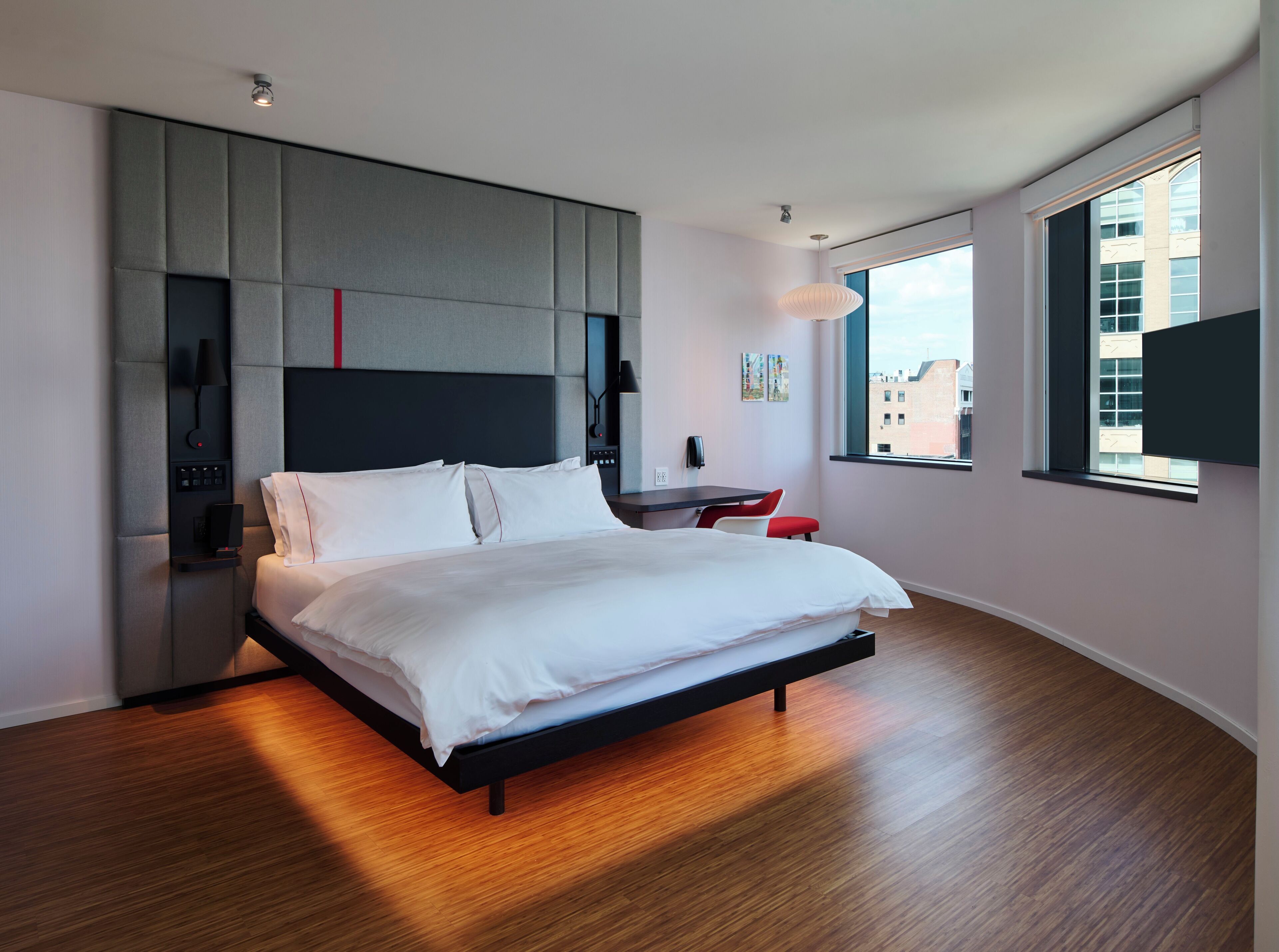 A modern hotel room with a large bed, a desk, and a view of the city through the window.