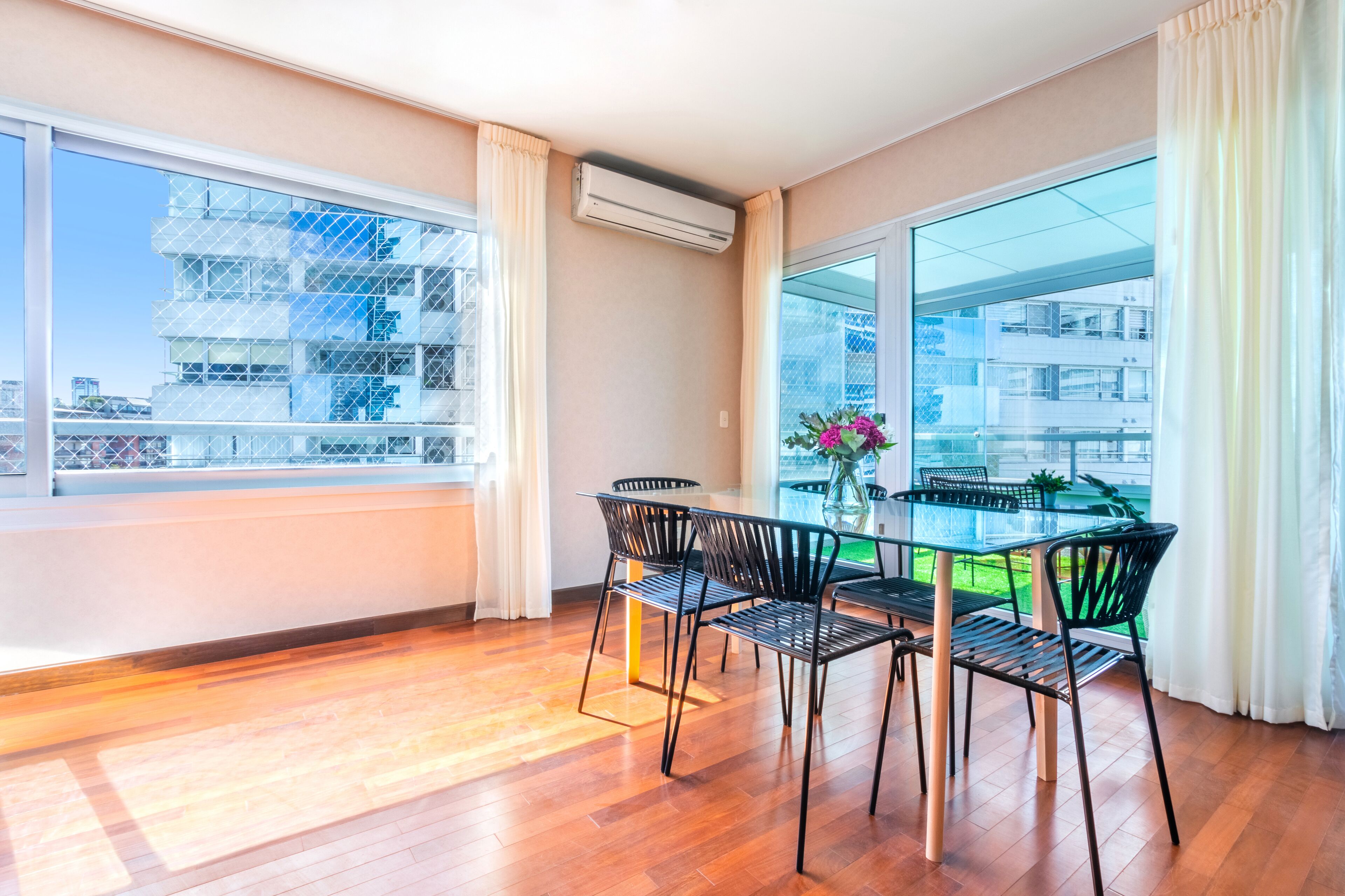 Una habitación moderna con una mesa de vidrio, sillas negras y vistas a un paisaje urbano a través de amplias ventanas.