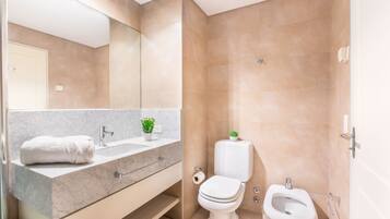 Un baño moderno con tocador de mármol, inodoro, bidé y un espejo grande.