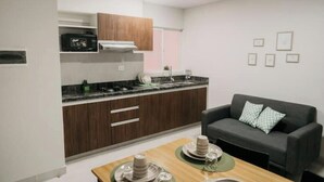 A compact kitchen with dark wooden cabinets, a built-in stove, and a grey sofa in the living area.