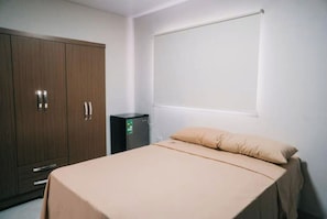 Un dormitorio con una cama, un armario y un electrodoméstico pequeño, probablemente un refrigerador.