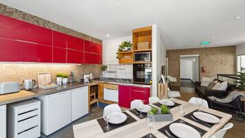 A modern kitchen with red cabinets, a dining area with a table set for four, and a living area with a sofa and a TV.