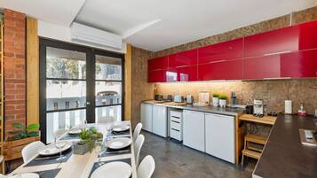 A modern kitchen with red cabinets, a dining area with white chairs, and a large window overlooking the city.