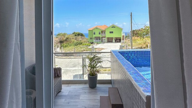 A balcony with a view of a green house, a swimming pool, and a potted plant. - The island Experience 2 bedroom apartment  (Castries)