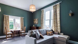 A living room with a sofa, a dining table with chairs, and a large window with curtains. - 1B Victorian Retreat in Chester (Cheshire West and Chester)