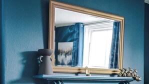 A room with a blue wall, a fireplace with a yellow brick surround, a mirror above the fireplace, and a plant in front of the fireplace. - ZooBlu: Chester 1-Bed (Cheshire West and Chester)