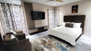 A modern bedroom with a large bed, a flat-screen TV mounted on the wall, and a ceiling fan. - TIES LUX VILLA COUPLE SUITES (La Fargue)