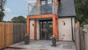 Une maison moderne à deux étages, dotée d’un balcon, d’une clôture en bois et de deux jardinières.