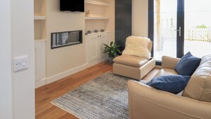 Un salon moderne comprenant un canapé, un fauteuil, un téléviseur à écran plat, un petit meuble et une plante en pot.
