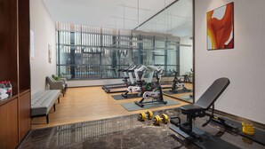 Une salle de sport moderne équipée de matériel d’exercice, d’un banc et d’une grande fenêtre donnant sur la ville.