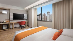 Une chambre d’hôtel avec un lit, un bureau avec une télévision, une chaise et une fenêtre donnant sur la ville.