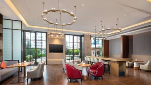 Un hall d’hôtel moderne avec un parquet en bois disposé en chevrons, des sièges rouges et blancs, un grand écran de télévision et de grandes fenêtres donnant sur l’extérieur.