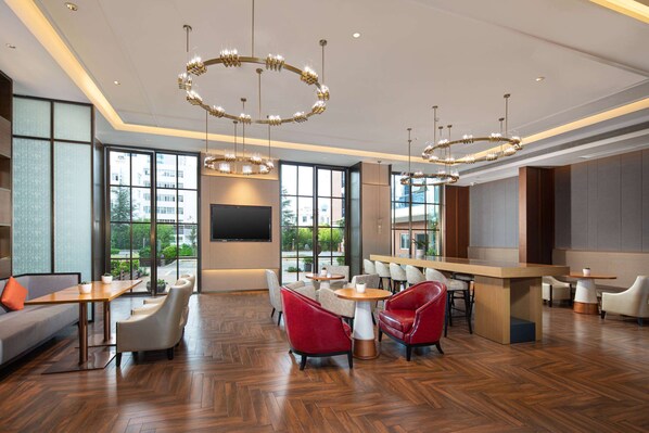 A modern hotel lobby with a herringbone wood floor, red and white seating, a large TV screen, and large windows offering a view of the outdoors. - Hawthorn by Wyndham Dali Erhai Park (Dali)
