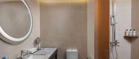A modern bathroom with a marble sink, a toilet, a glass-enclosed shower, and a round mirror.
