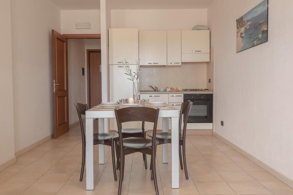 Une cuisine compacte avec des meubles blancs, une table à manger avec des chaises et un petit îlot central agrémenté d’un vase.