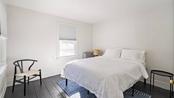 Un dormitorio con una cama, una silla, una lámpara y un radiador.