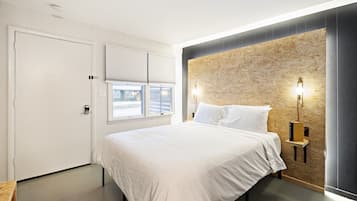 Un dormitorio con cama, ventana con persianas, lámpara de pared y puerta.