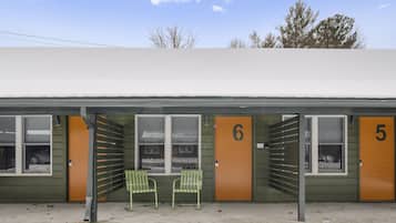 A motel with numbered doors, a covered waiting area, and two green chairs.