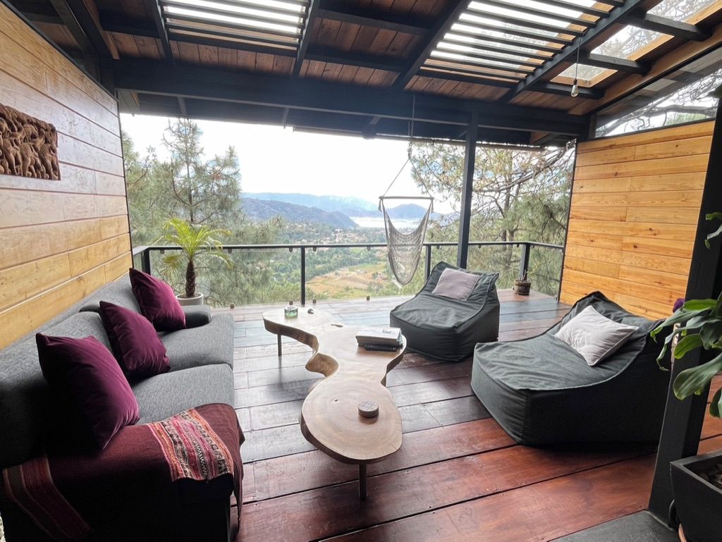 Un espace extérieur aménagé avec une zone salon couverte, comprenant un canapé, deux fauteuils poire et une table en bois originale.