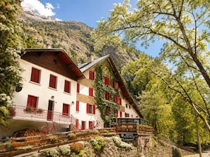 A traditional mountain hotel with a wooden facade, red shutters, and a balcony with a view of the surrounding landscape. - Hotel Au Bon Accueil (Les Deux Alpes)
