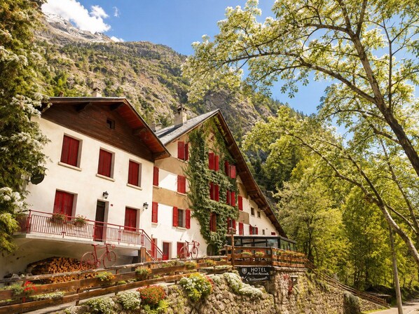 A traditional mountain hotel with a wooden facade, red shutters, and a balcony with a view of the surrounding landscape. - Hotel Au Bon Accueil (Les Deux Alpes)