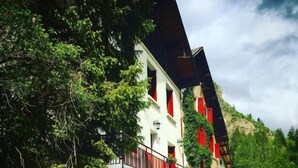 Un chalet traditionnel avec un escalier en bois, un balcon doté de rampes rouges et un jardin fleuri.