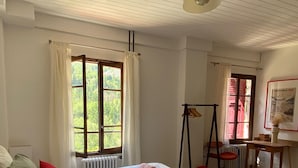 A room with two beds, a radiator, a desk, a chair, a lamp, and a window with curtains. - Hotel Au Bon Accueil (Les Deux Alpes)