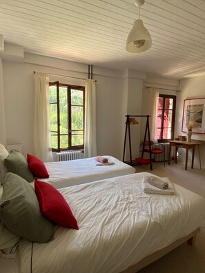 Ein Zimmer mit zwei Betten, einem Heizkörper, einem Schreibtisch, einem Stuhl, einer Lampe und einem fenster mit Vorhängen.