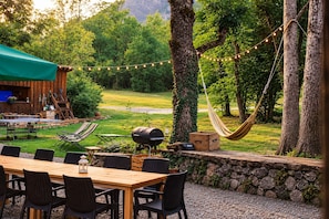An outdoor patio with a wooden table and chairs, a hammock, and a barbecue grill. - Hotel Au Bon Accueil (Les Deux Alpes)