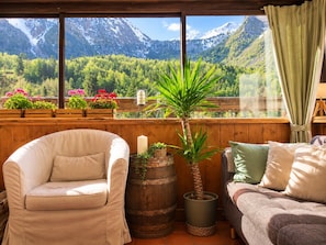 A cozy room with a view of mountains, a wooden chair, a sofa, and potted plants. - Hotel Au Bon Accueil (Les Deux Alpes)