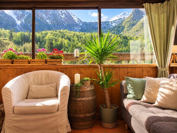 A cozy room with a view of mountains, a wooden chair, a sofa, and potted plants. - Hotel Au Bon Accueil (Les Deux Alpes)