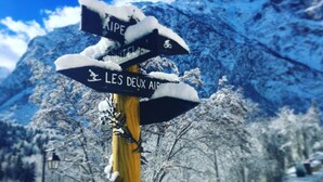 A signpost with directional arrows and text in a snowy landscape. - Hotel Au Bon Accueil (Les Deux Alpes)