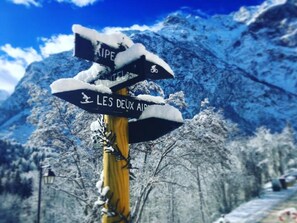 A signpost with directional arrows and text in a snowy landscape. - Hotel Au Bon Accueil (Les Deux Alpes)