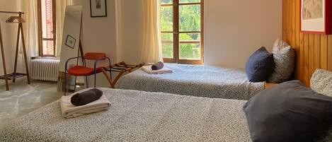 A room with two beds, a chair, a radiator, a window, and a ceiling light.