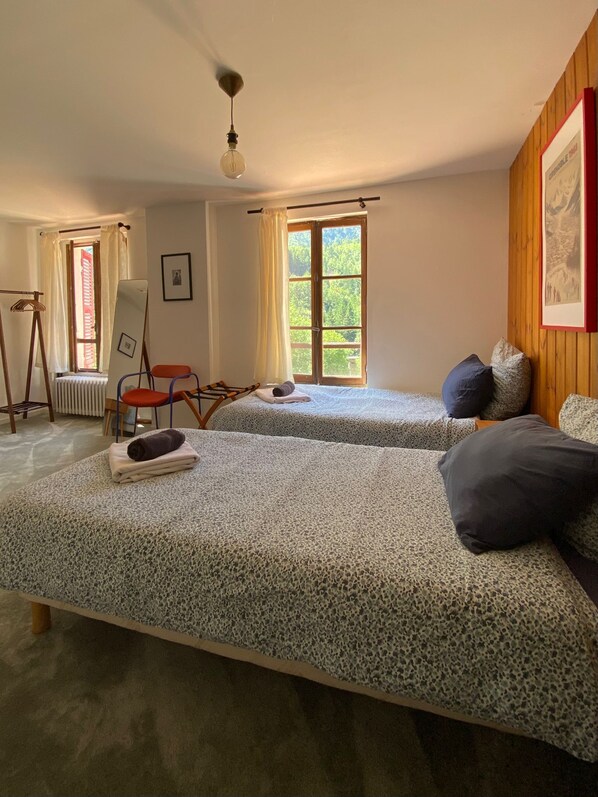 Ein Zimmer mit zwei Betten, einem Sessel, einer Heizung, einem Fenster und einer Deckenleuchte.