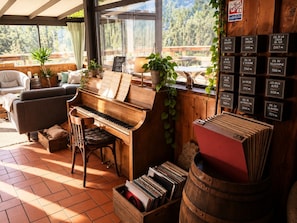 A cozy room with a piano, a couch, and a view of the forest. - Hotel Au Bon Accueil (Les Deux Alpes)