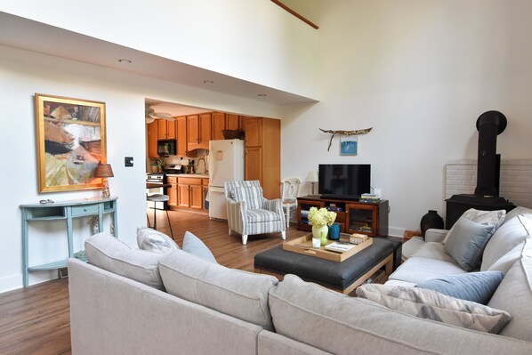 A living room with a sofa, armchair, and a television. There is a kitchen in the background with wooden cabinets and a refrigerator. - Walk to the beach from this cozy birder cottage! 3beds, 2ba (Cape May Point)