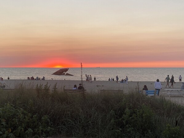 Eine Strandansicht, zeigt Menschen, die sich entspannen und am Ufer entlanggehen, während die Sonne untergeht.