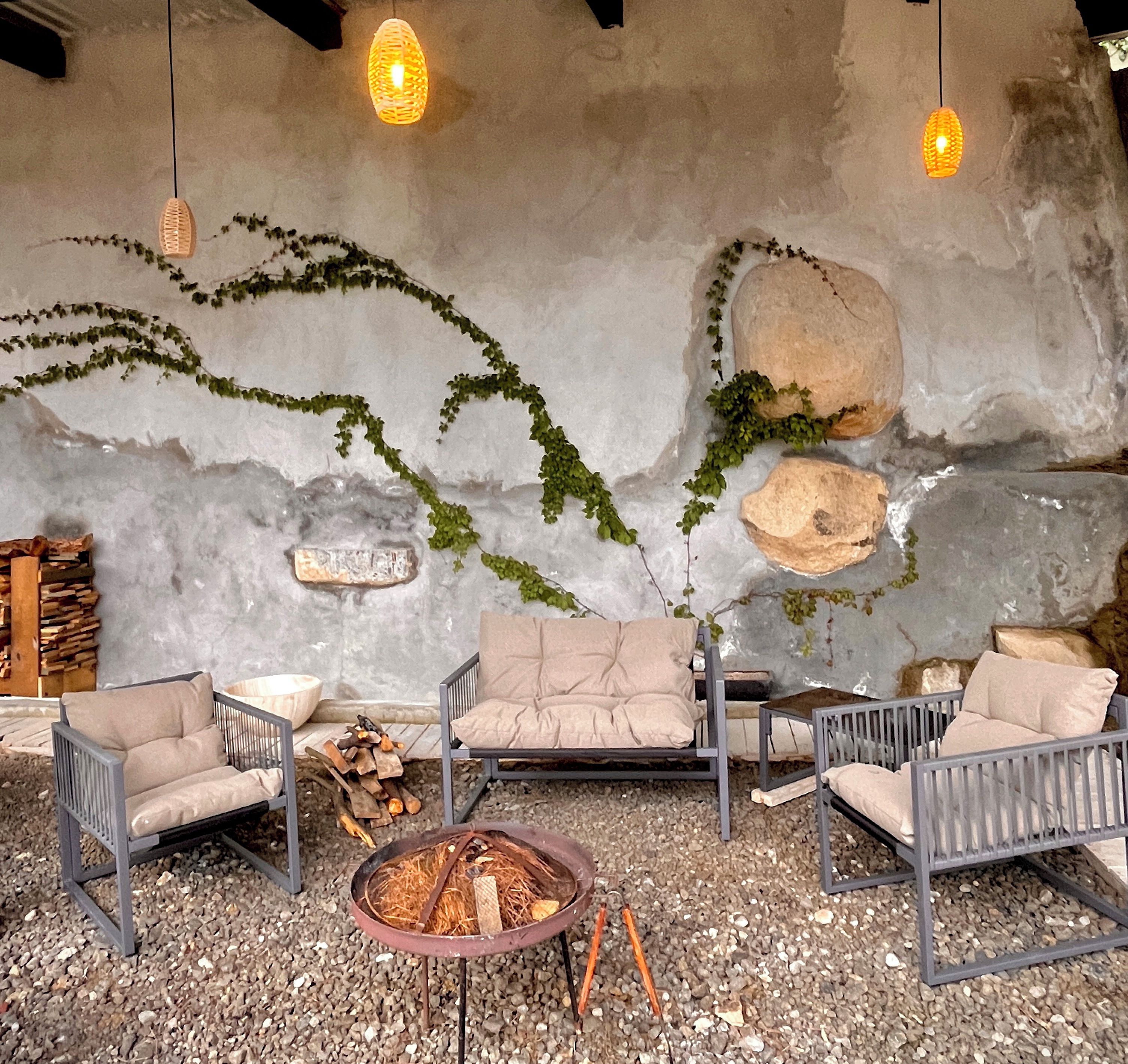 A cozy seating area with a fire pit, stone wall, and hanging lights.