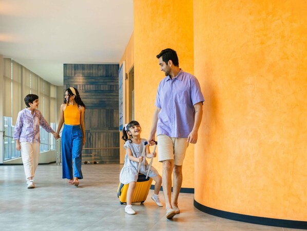 Une famille se promène dans un couloir d’hôtel au design moderne, doté de grandes fenêtres et d’un mur incurvé.