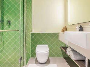 A bathroom with a toilet, a shower, and a sink with toiletries. - Ibis Styles Goa Vagator (Vagator)