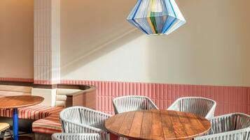 A dining area with a round wooden table surrounded by white wicker chairs, a striped bench, and a colorful hanging light fixture.
