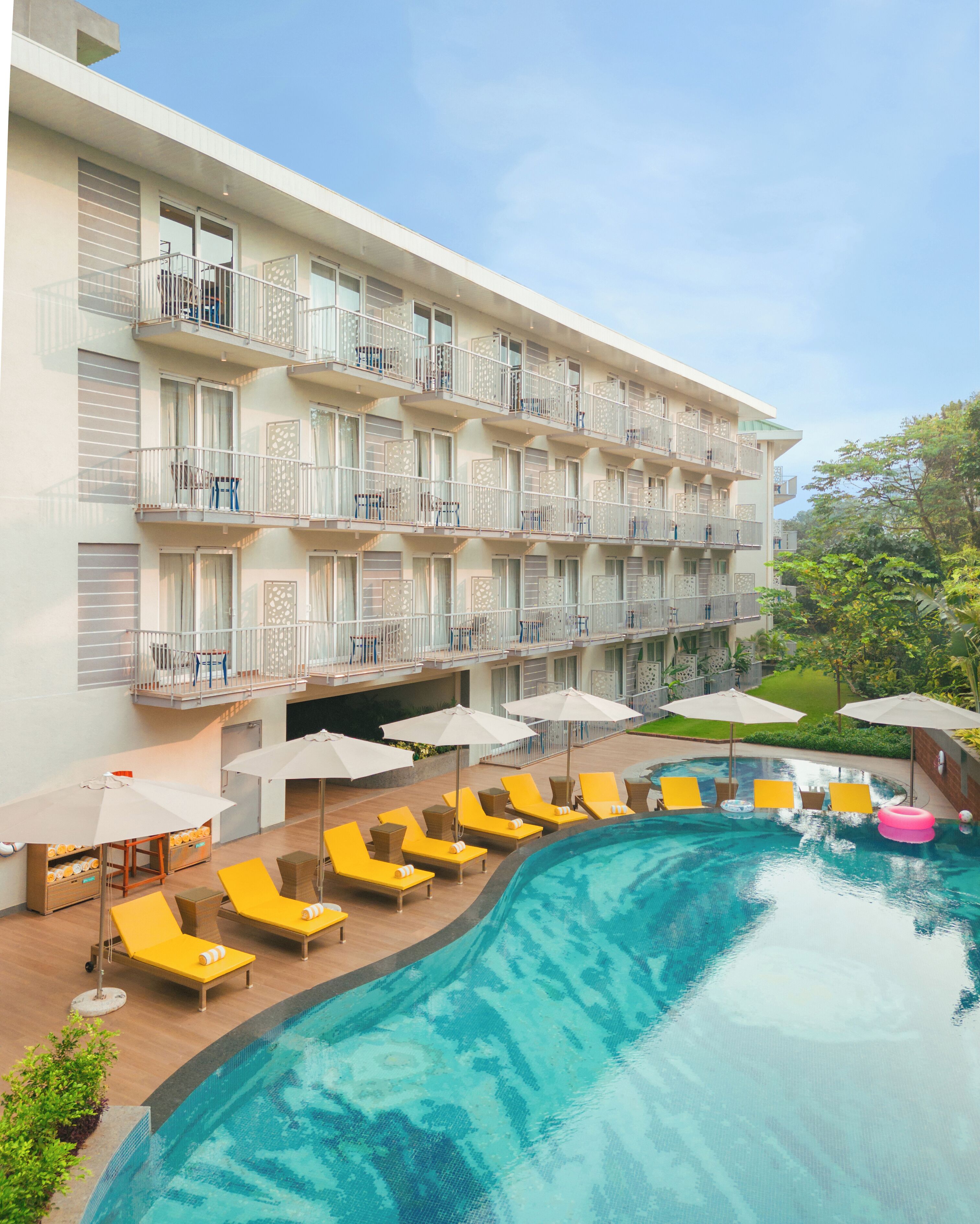 A hotel with a swimming pool surrounded by yellow lounge chairs and umbrellas.