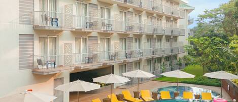 A hotel with a swimming pool surrounded by yellow lounge chairs and umbrellas.